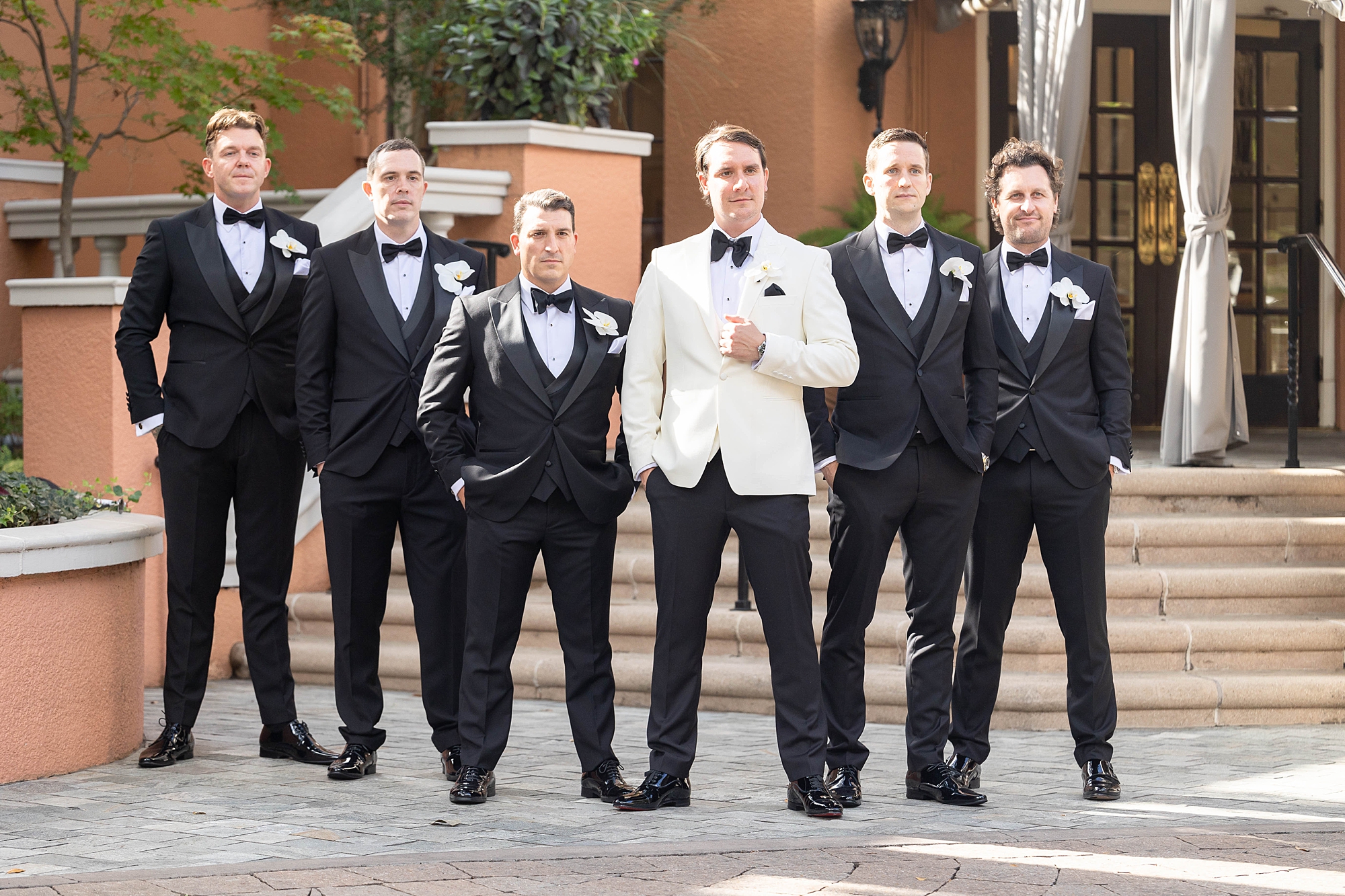 groom in white suit jacket stands with groomsmen in tuxes in Dallas TX