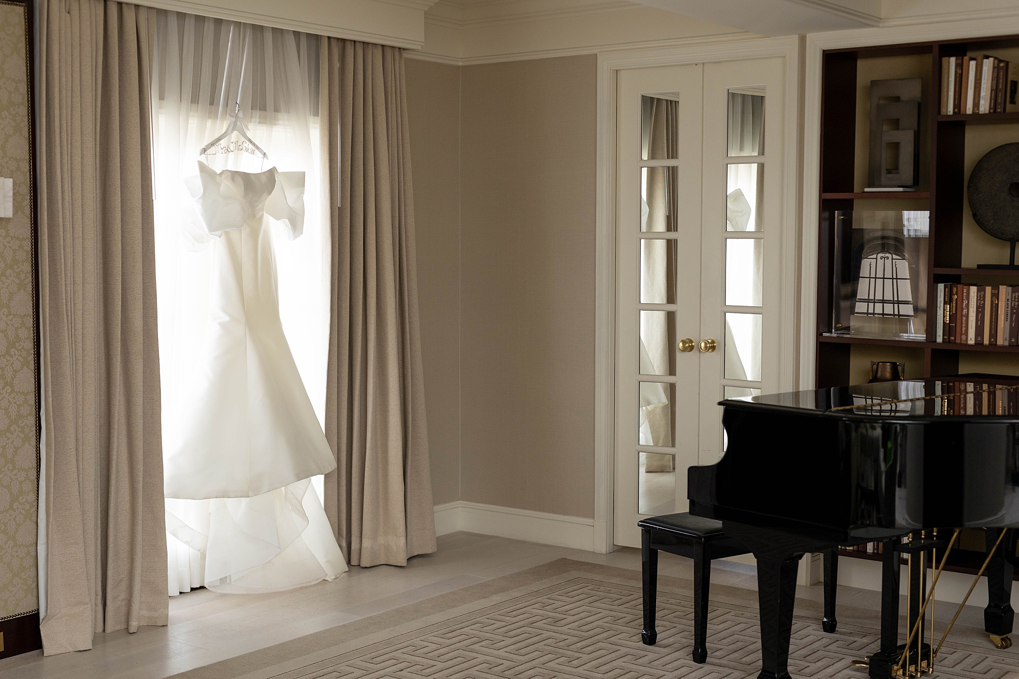 wedding dress hangs in room at Rosewood Mansion with piano next to it 