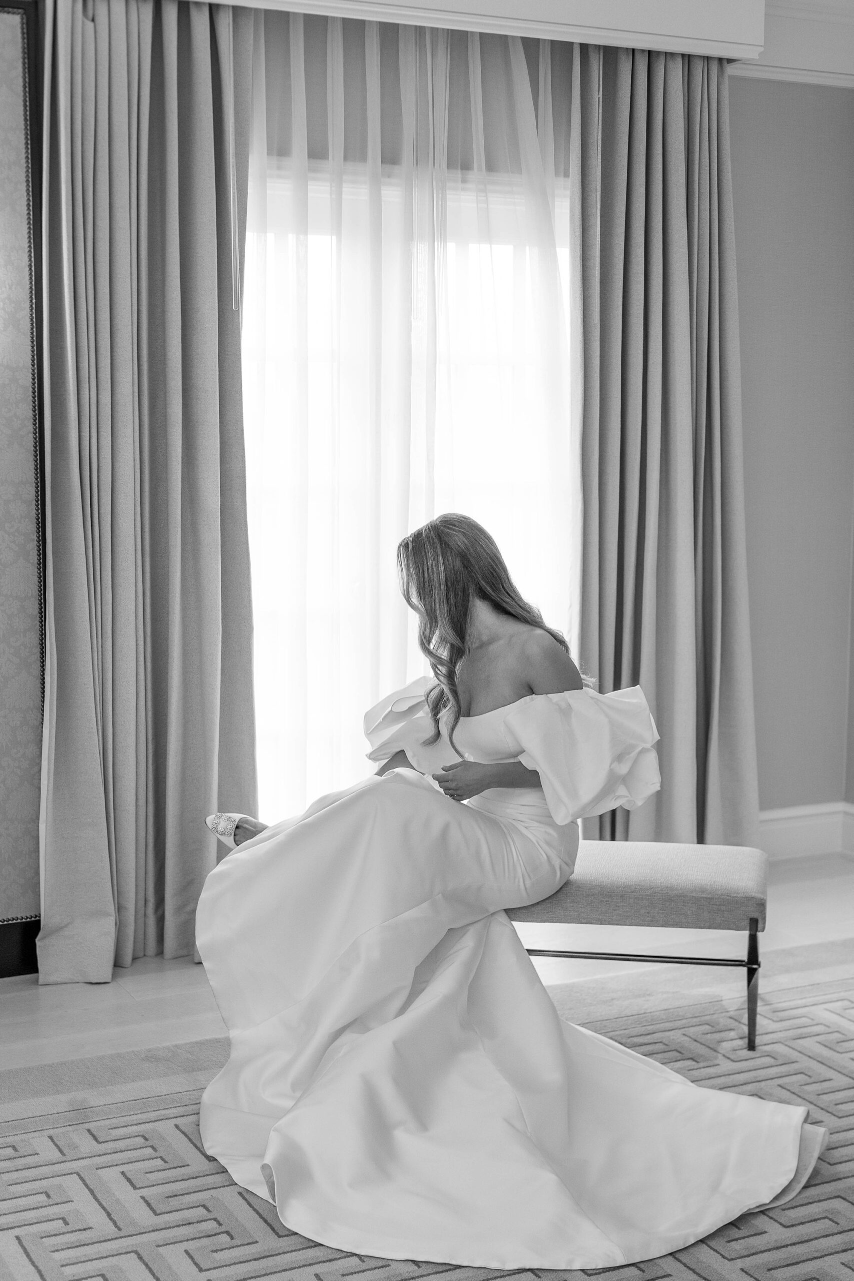 bride with off-the-shoulder wedding gown puts shoes on before Dallas wedding day