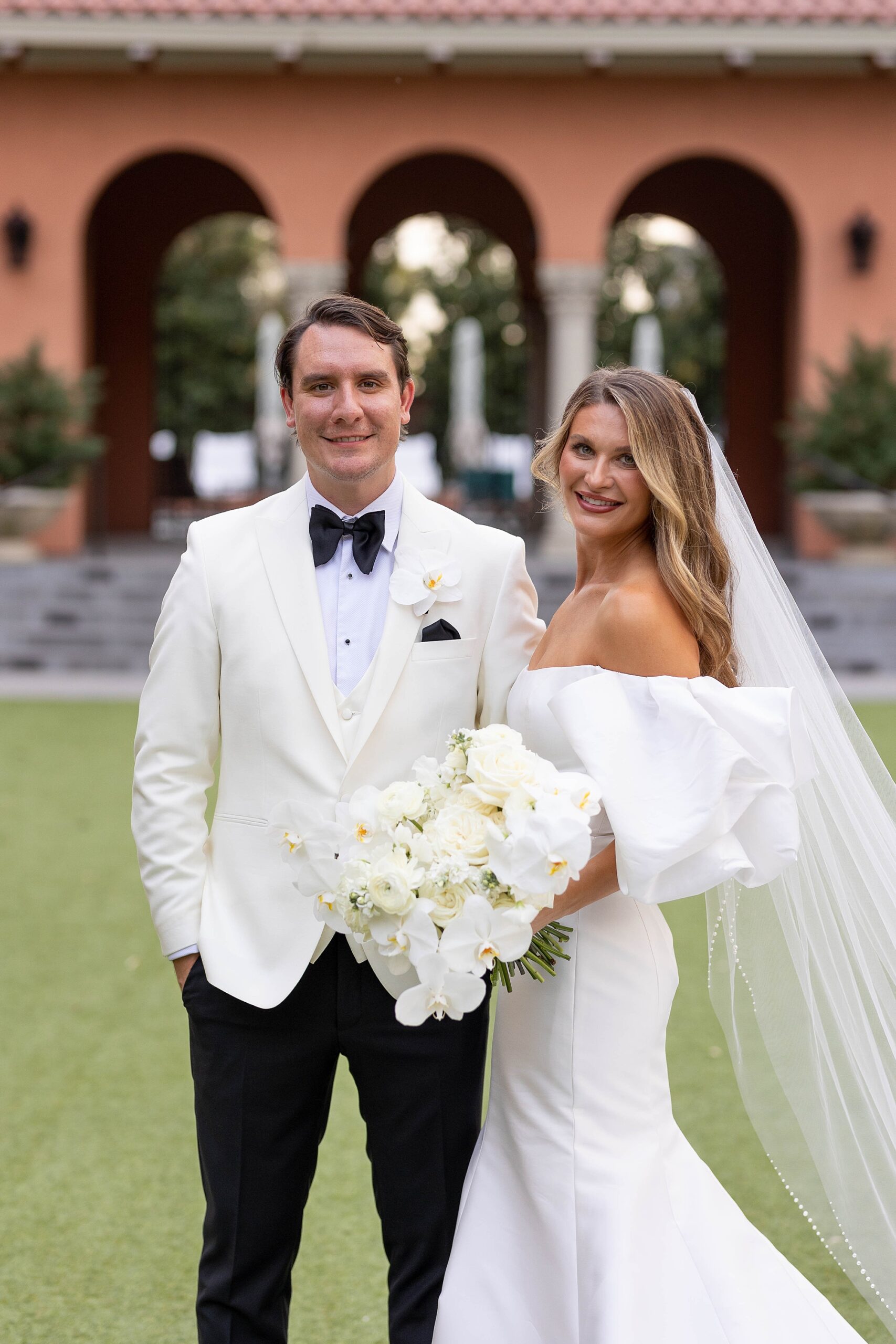 bride holds groom's arm in white tux jacket outside Rosewood Mansion
