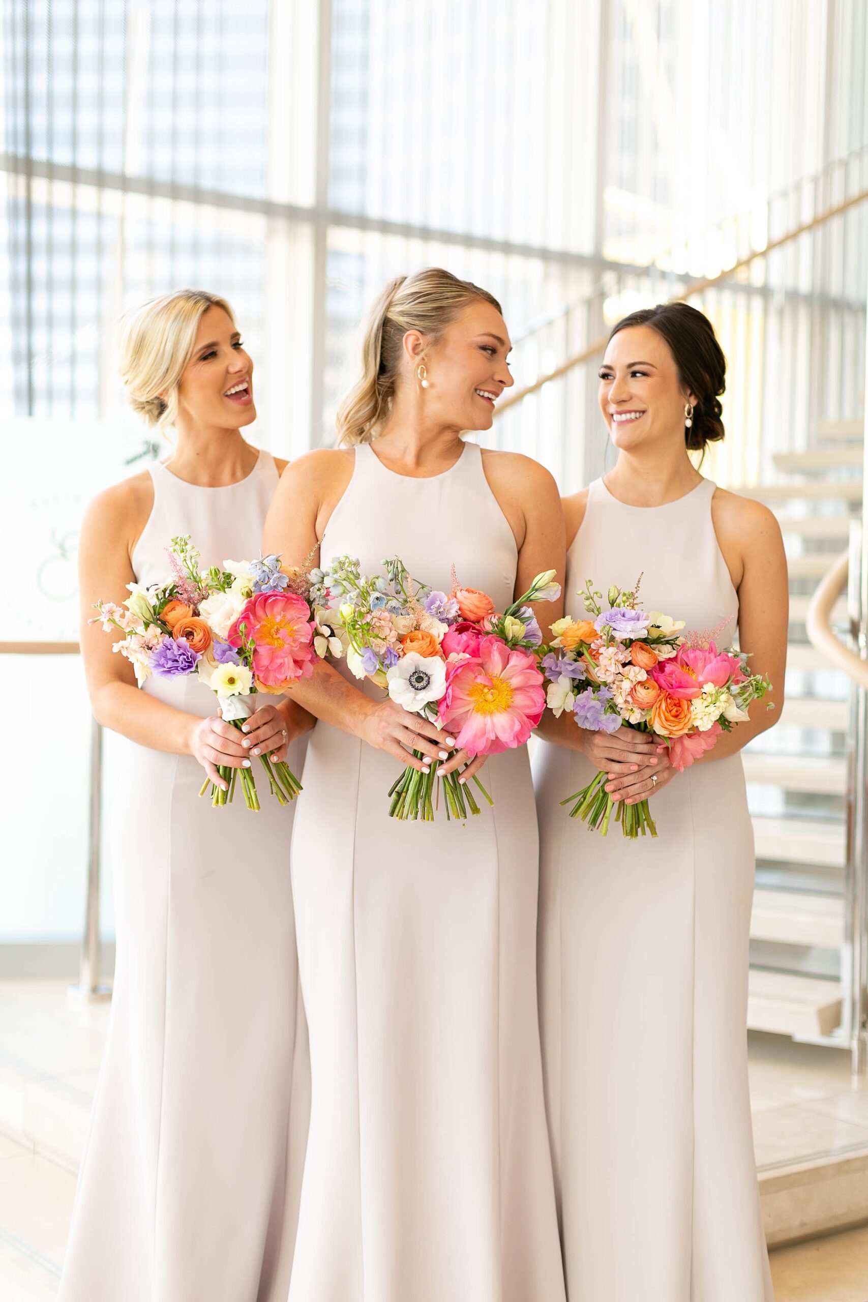bridesmaids in ivory gowns hold bright summer bouquets for wedding
