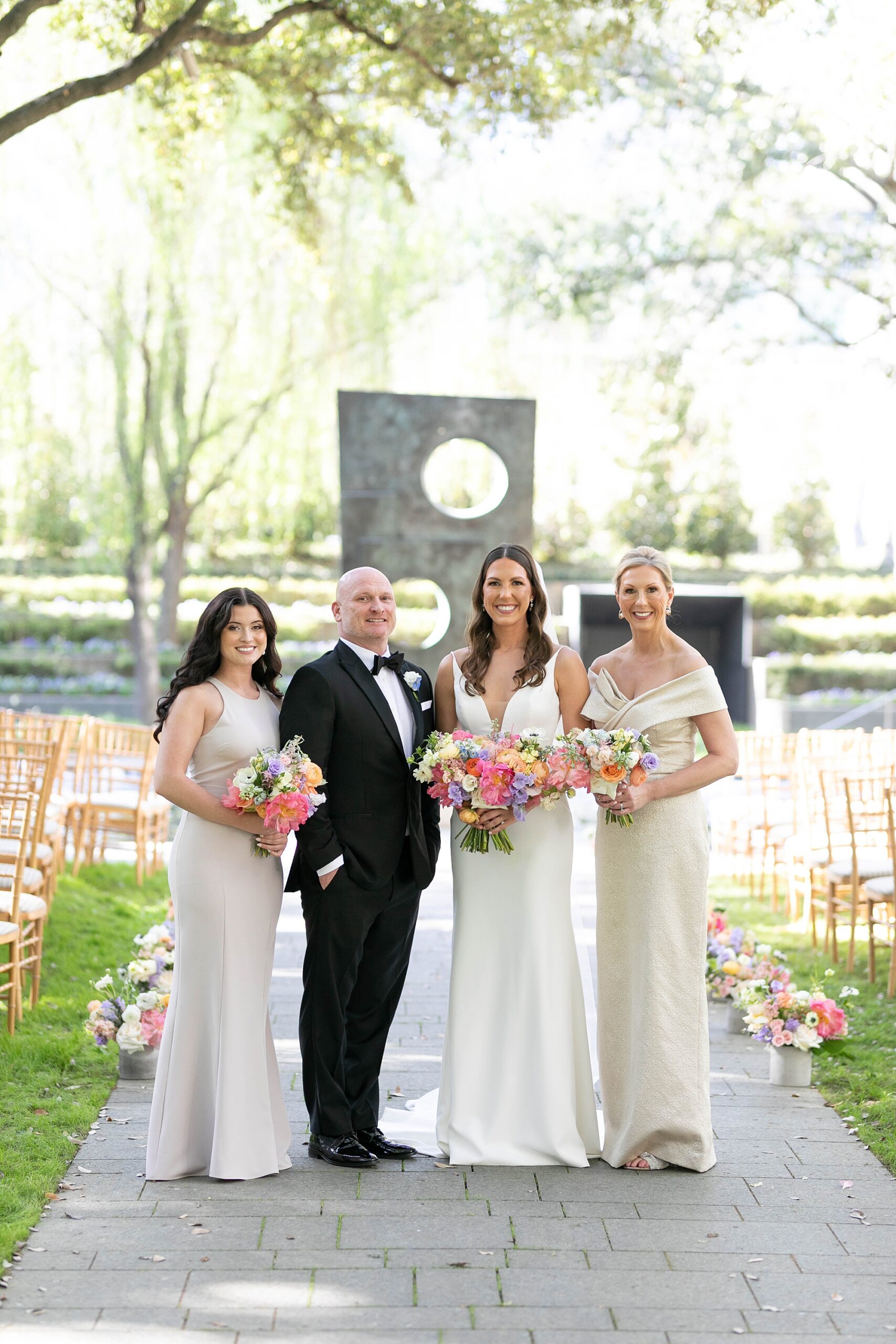 bride poses with family in front of tall sculpture in gardens