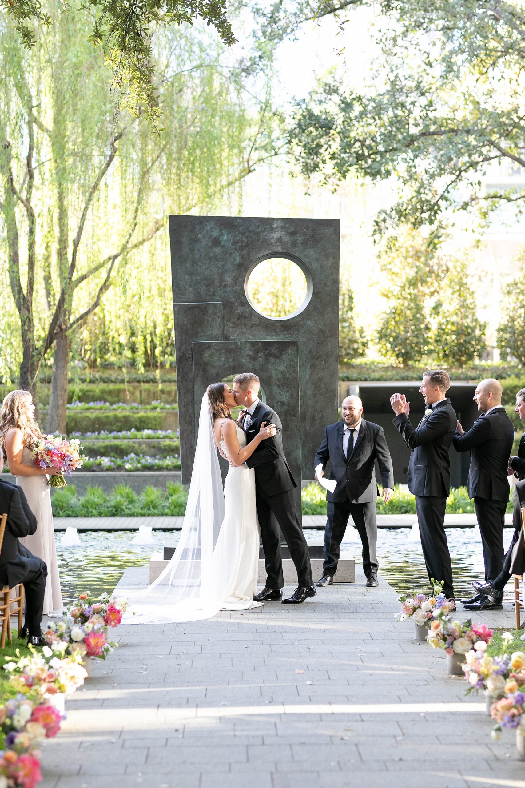 bride and groom kiss in front of tall grey sculpture during ceremony inside the Nasher Sculpture Center