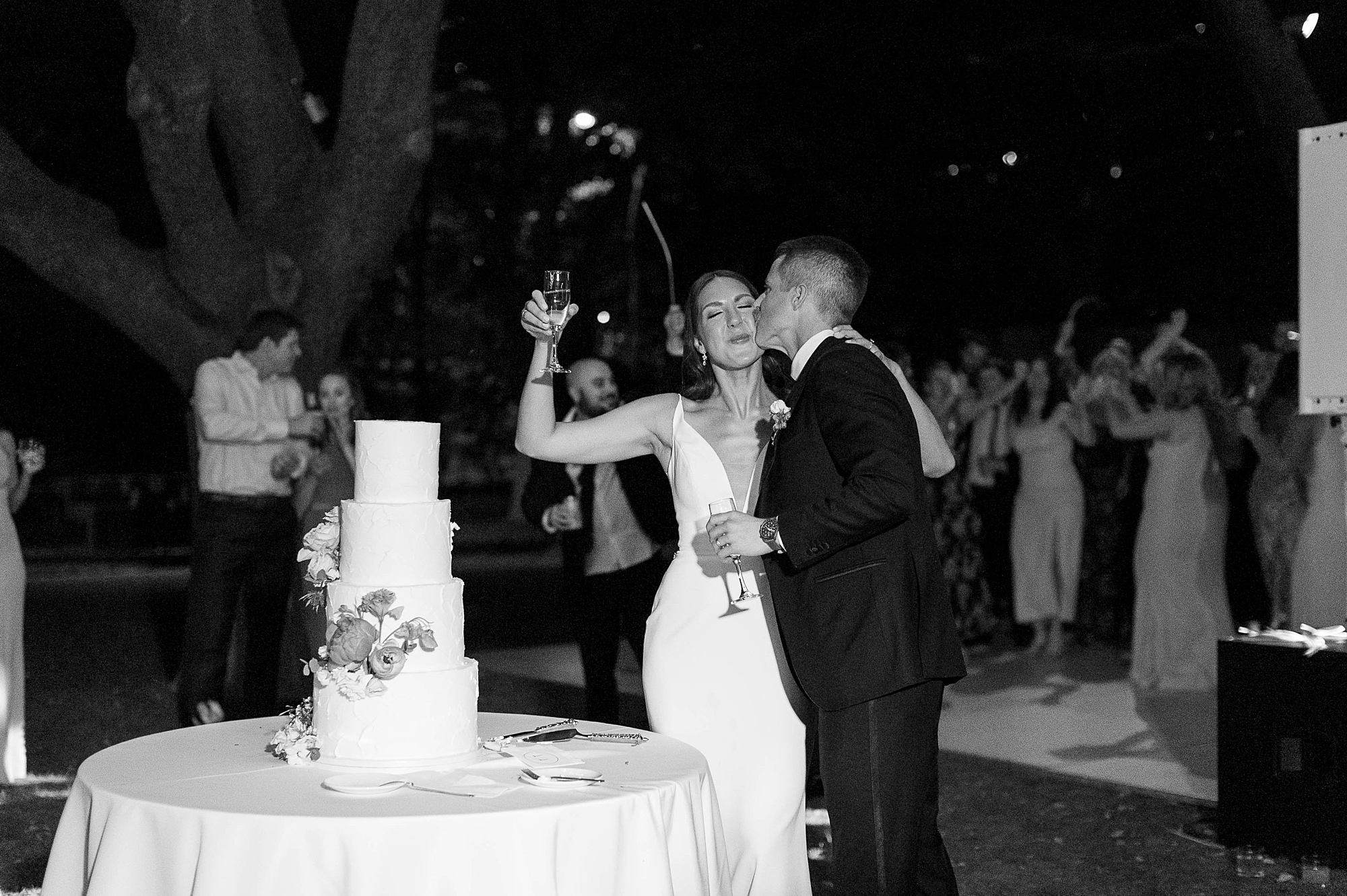 groom leans to kiss bride's cheek during cake cutting at al fresco wedding reception at the Nasher Sculpture Center