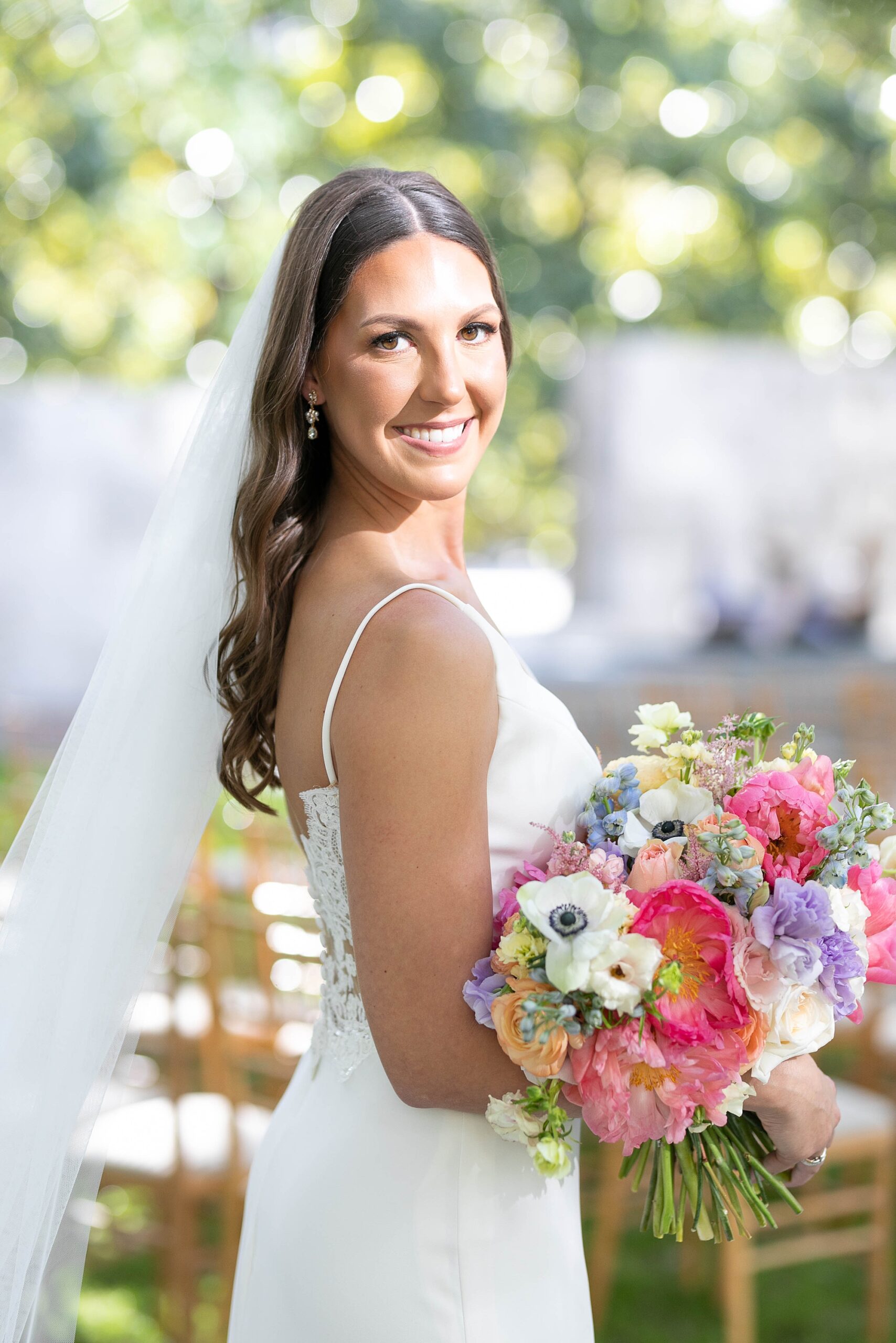 bride looks over shoulder holding bouquet of bright flowers at the Nasher Sculpture Center