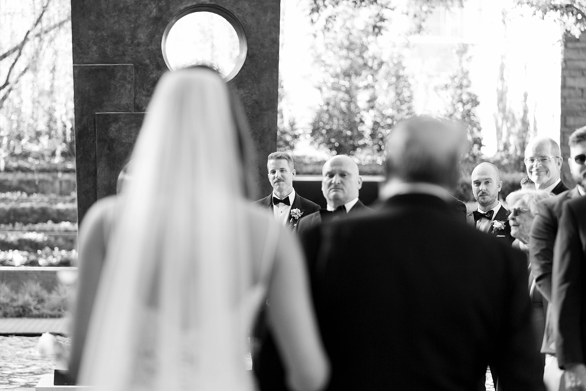 photo of groom over bride's shoulder as she walks down aisle 