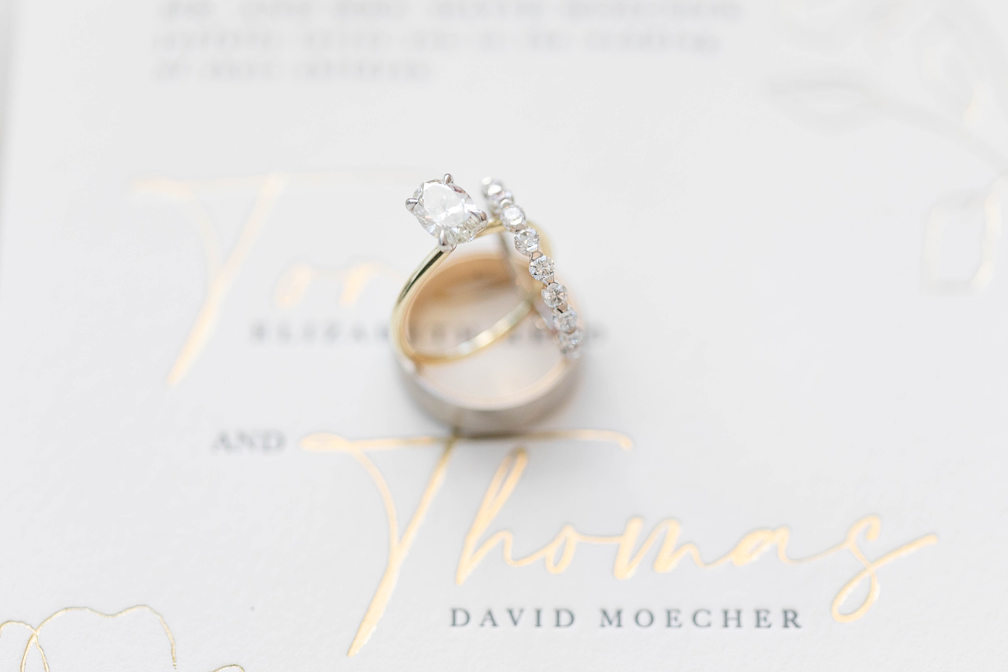 three wedding rings lay stacked on gold and white invitation 