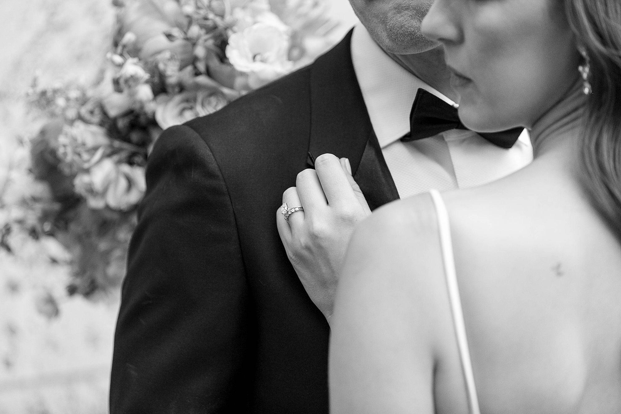 bride leans into groom holding his lapel showing off wedding rings 
