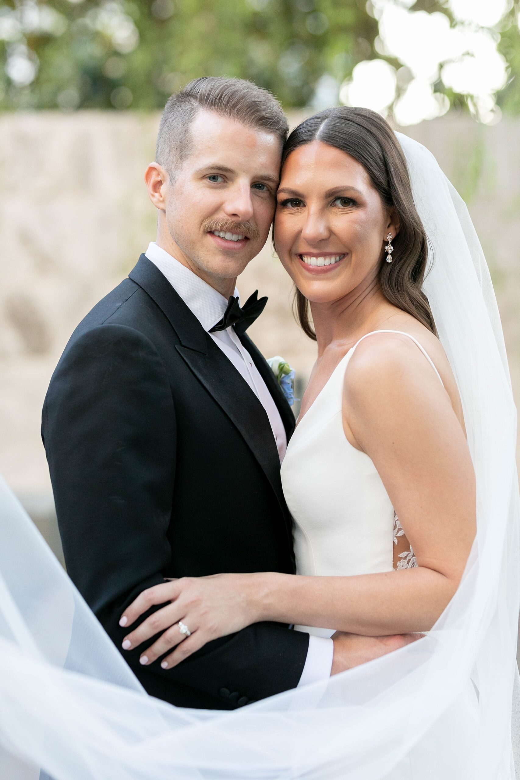newlyweds lean heads together while bride's veil wraps around them 