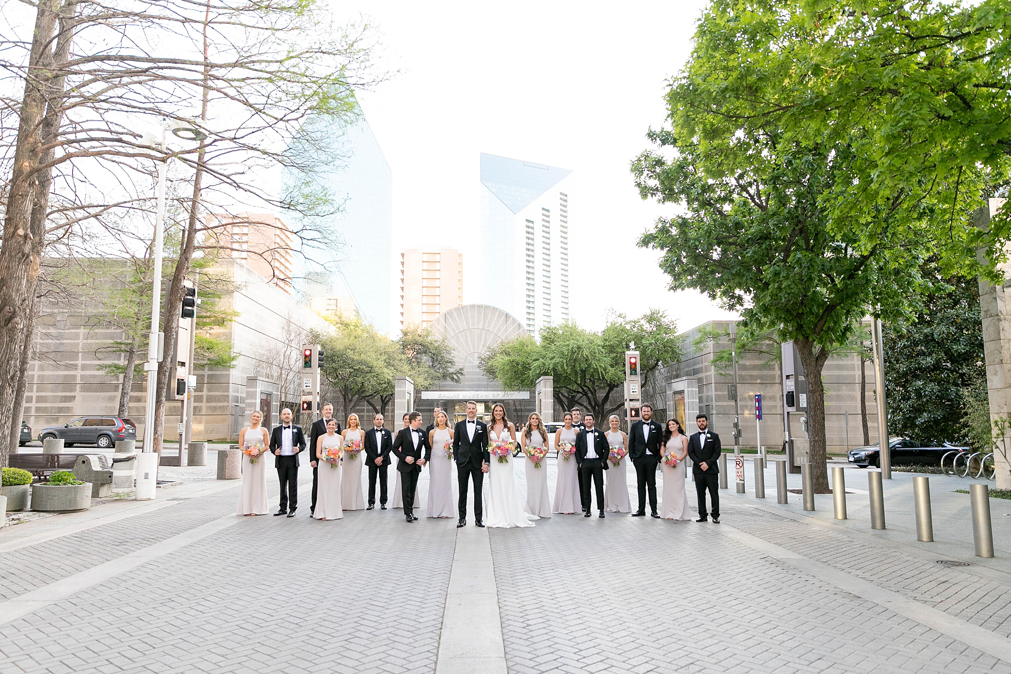 bride and groom walk on street with wedding party outside the Nasher Sculpture Center