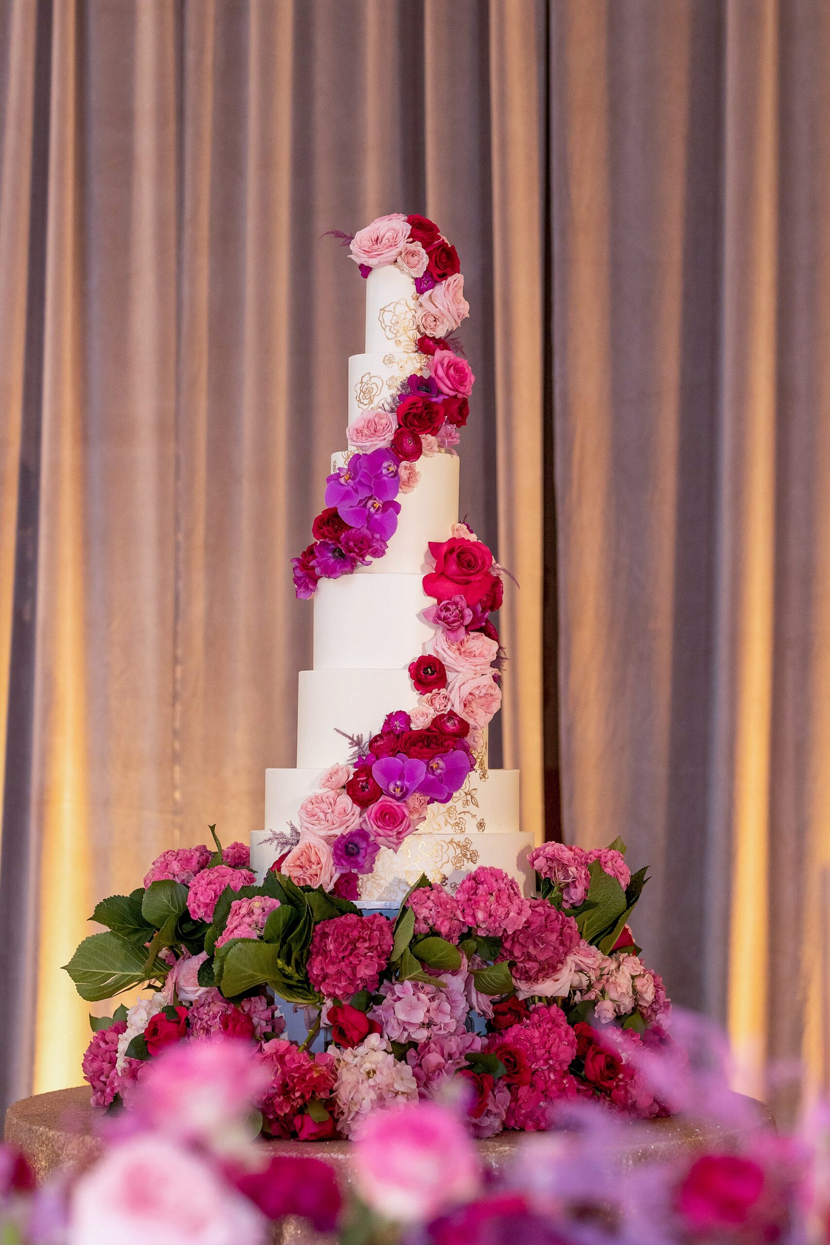 tiered wedding cake with pink flowers winding around tiers 